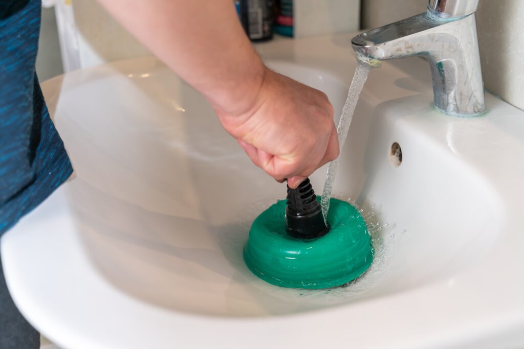 man unclogging a blocked drain with a green plunger