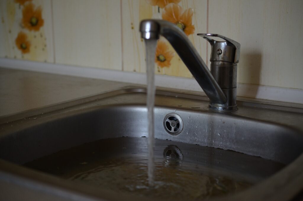 Stainless steel sink plug hole close up full of water and particles of food
